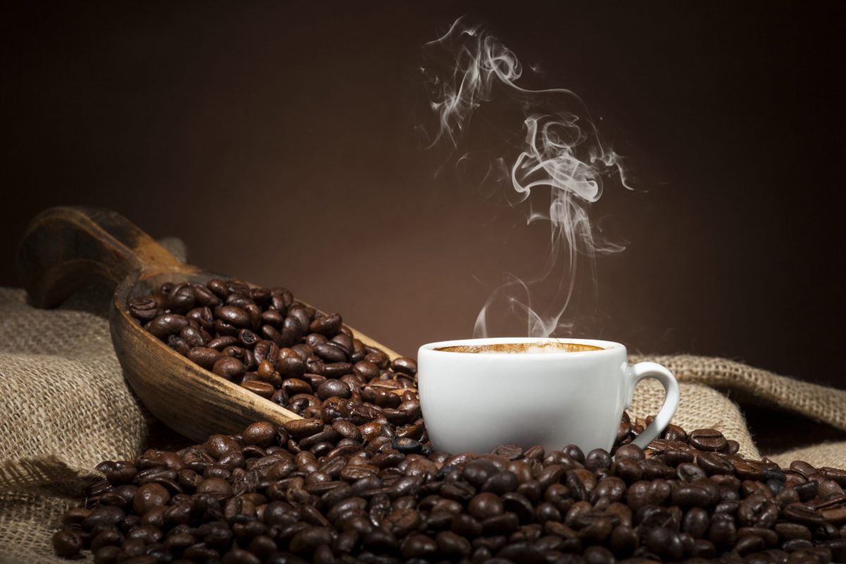 White coffee cup and coffee beans on burlap textile and brown background.